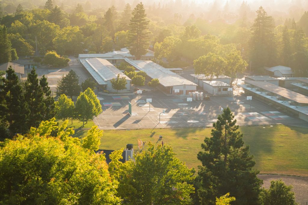 Scenic aerial image of a school complex surrounded by lush greenery at sunset.